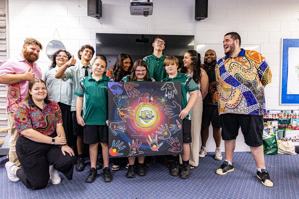 A group of staff and students displaying a painting with coloured hand prints.